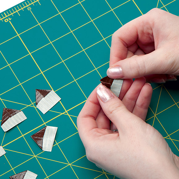 squares from previous step with the top two corners folded to the center to form a double sided triangle with a sticky rectangle sticking out the bottom